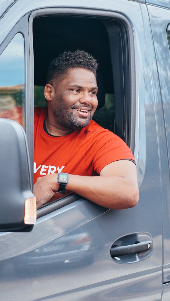 Happy delivery driver in red shirt smiling out van window, creating a positive delivery service vibe.